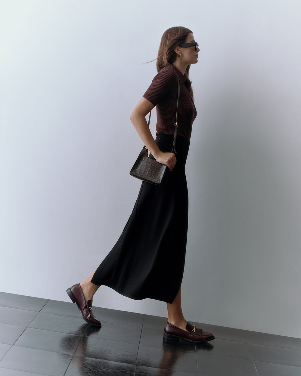 Woman in skirt and shirt carrying croc-embossed leather purse across her shoulder.