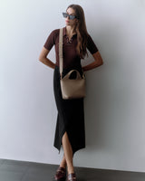 Woman wearing sunglasses, a top, a long skirt, and carrying a shoulder bag