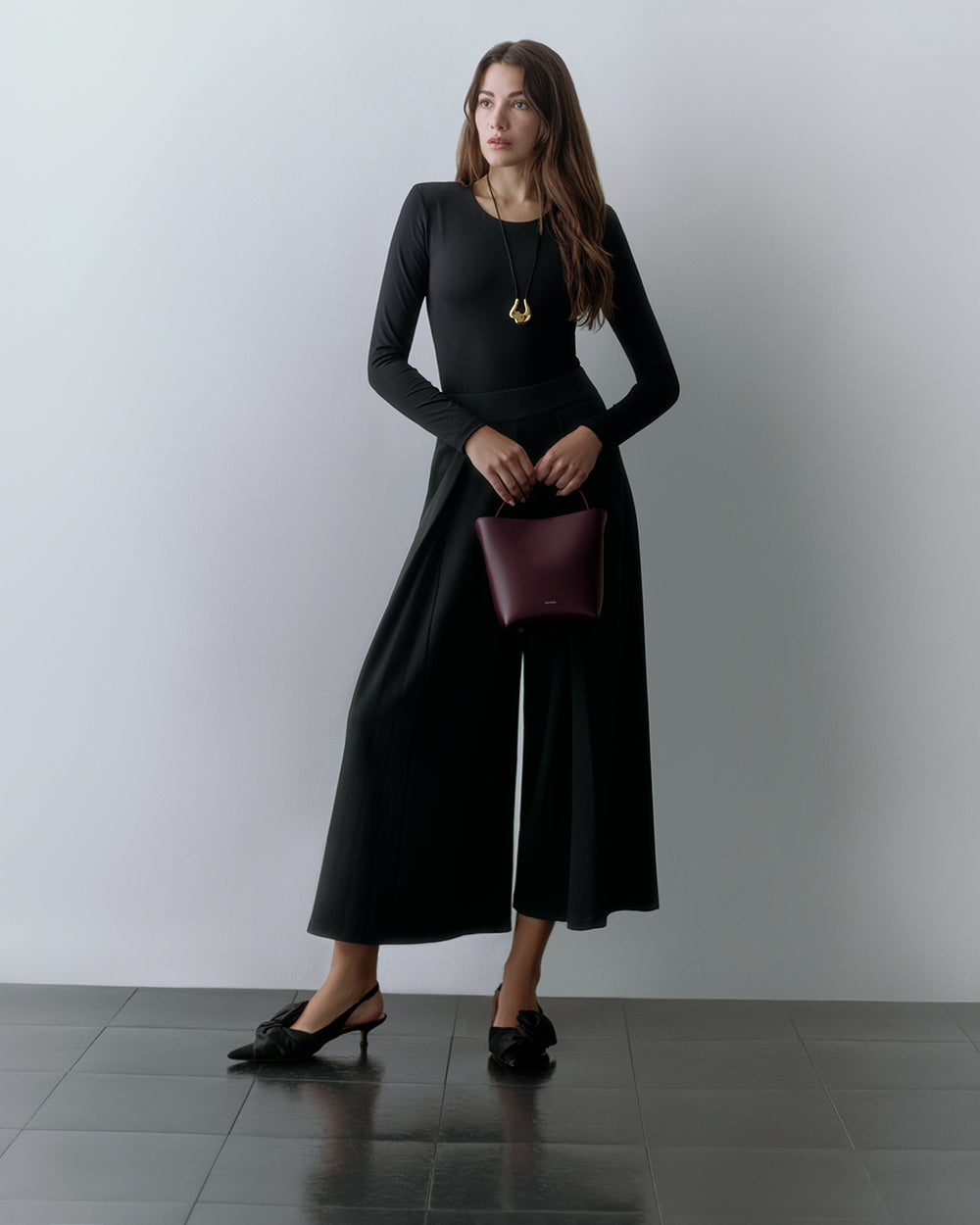 Person in outfit holding a small bag standing on a tiled floor.