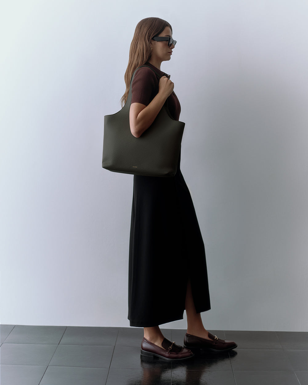 Person with sunglasses carrying a large handbag, wearing a long skirt and loafers