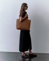 Person wearing sunglasses and holding large tote bag, dressed in long skirt and loafers.