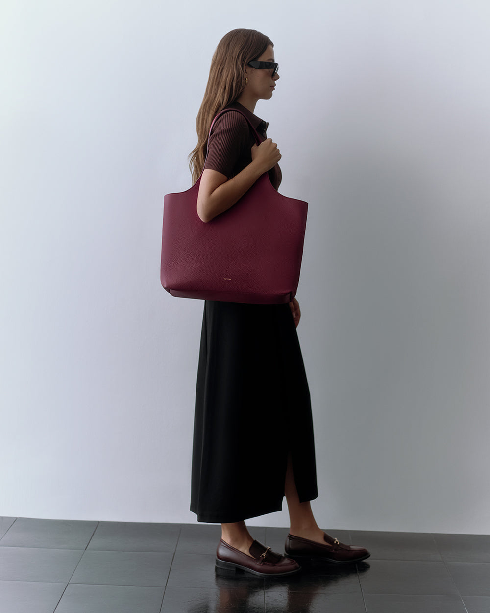 Person standing sideways holding a large tote bag, wearing a long skirt and shoes