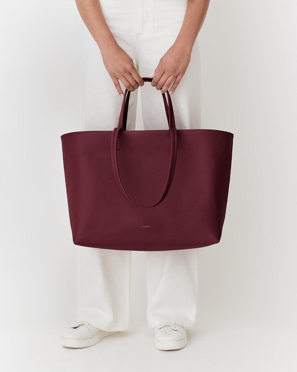 Person holding a large tote bag, wearing light pants and shoes.