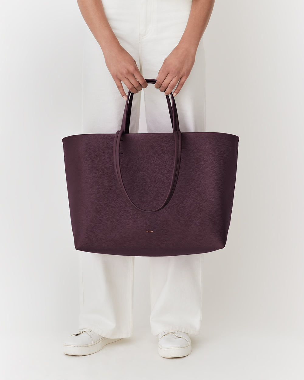 Person holding large tote bag, wearing long pants and shoes.