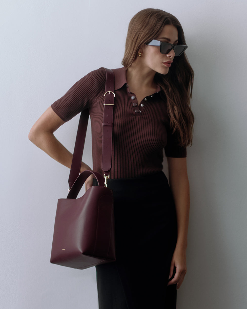 Woman with sunglasses carrying a handbag over shoulder, wearing a short-sleeve top and skirt.