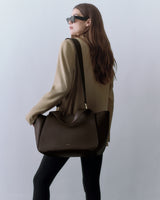 Person wearing sunglasses and holding a large handbag on shoulder.