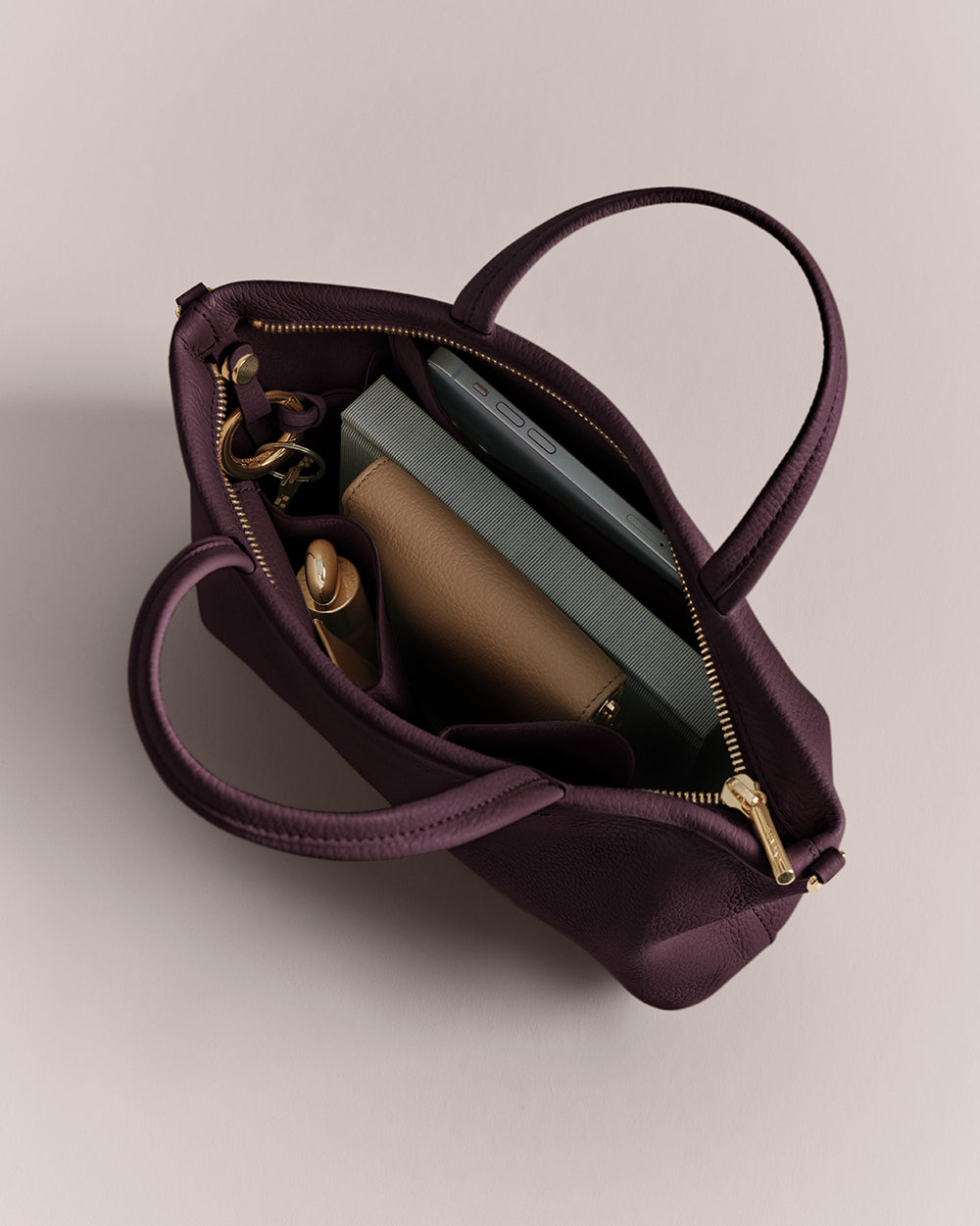 Open handbag with phone, book, wallet, and a small bottle inside