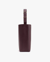 Side view of a tall leather bag with a single strap and buckle.