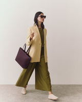 Person in blazer and wide pants holding a handbag, walking confidently.