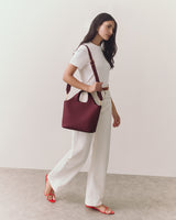 Woman in white outfit carries a shoulder bag, walking in red sandals.