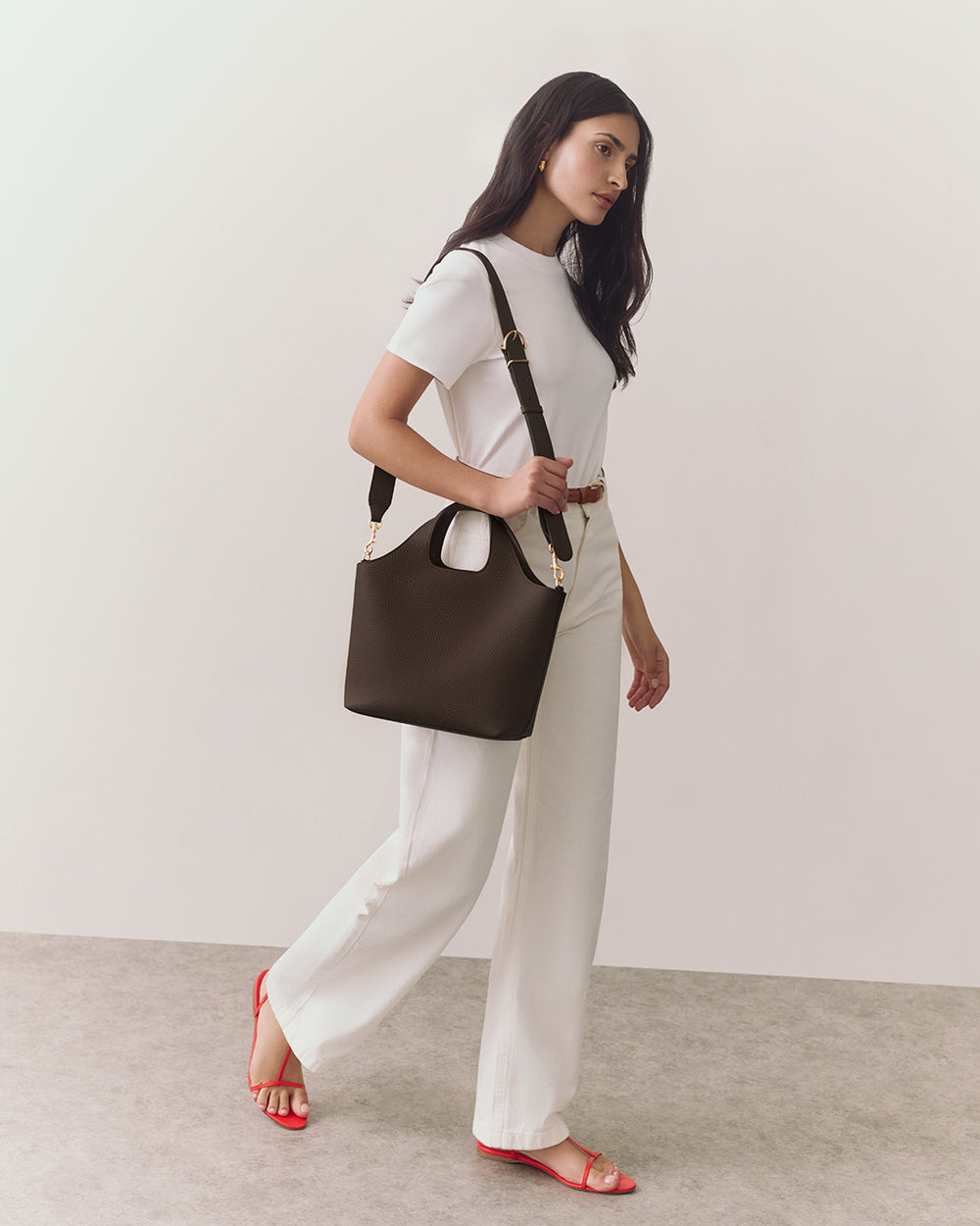 Person walking with a handbag, wearing a shirt, pants, and sandals.