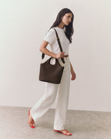 Person walking with a handbag, wearing a shirt, pants, and sandals.
