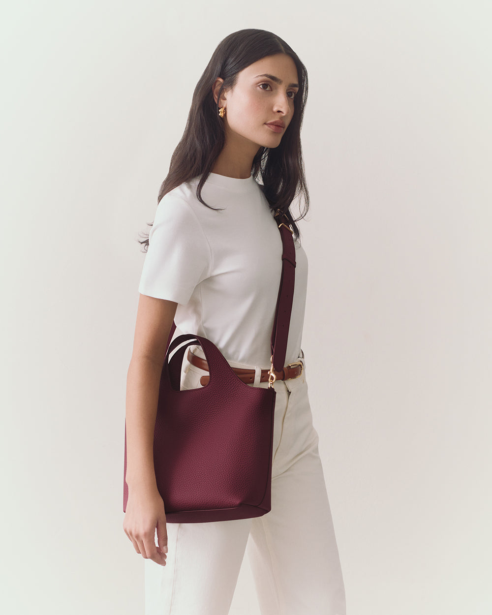 Woman wearing a plain shirt and pants, holding a handbag, with a strap over shoulder.