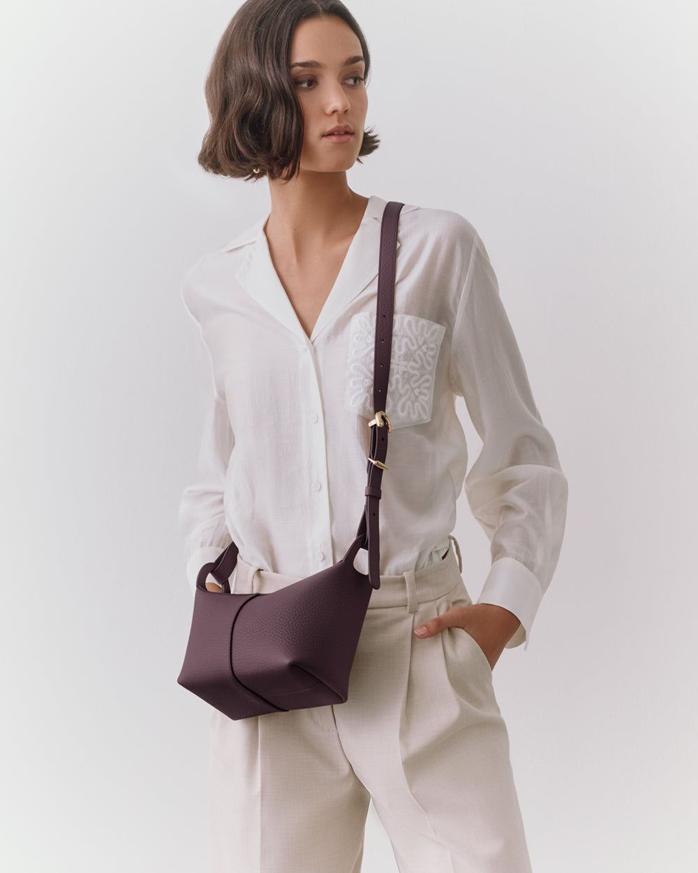 Person wearing a white shirt and trousers, holding a shoulder bag.