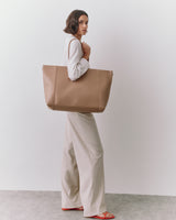 Person holding large tote bag, wearing long-sleeve top and wide-leg pants