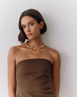 Person wearing strapless top and chain necklace standing against plain background