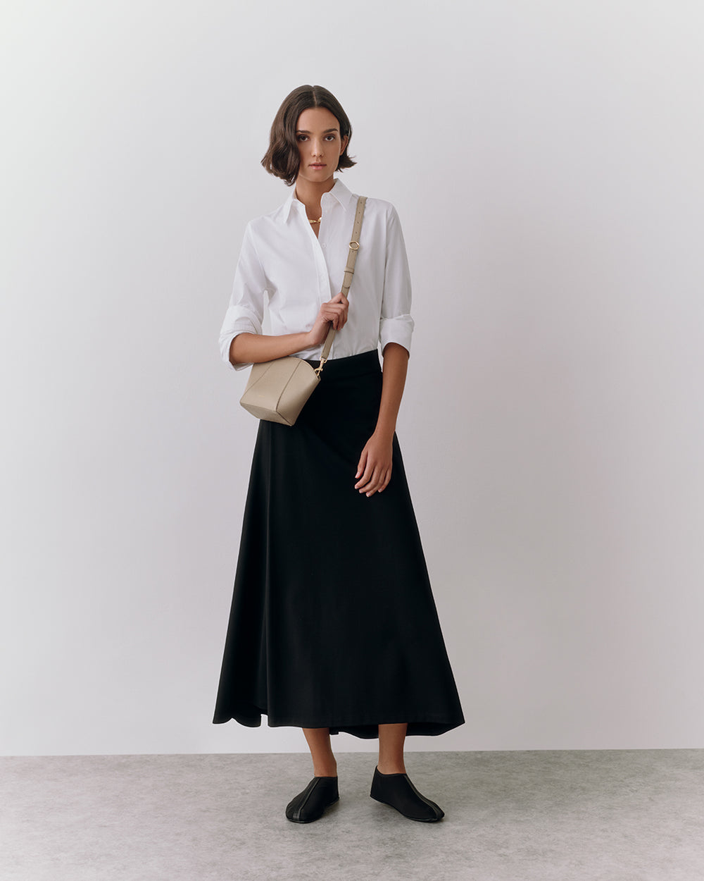 Person wearing a long skirt and shirt, holding a small bag over shoulder.