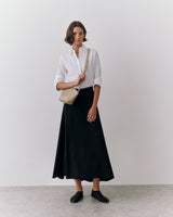 Person wearing a long skirt and shirt, holding a small bag over shoulder.