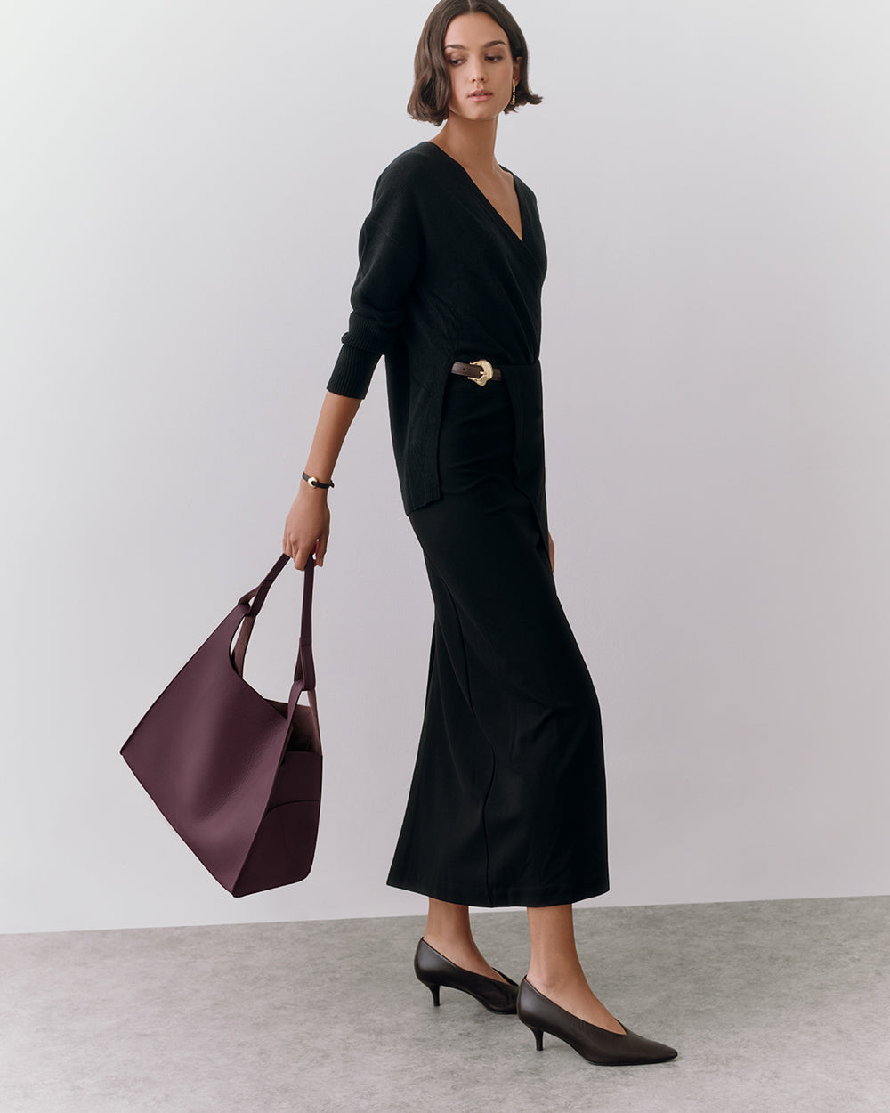 Person in long sleeve outfit holding a large handbag, wearing heels.
