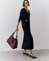 Person in long sleeve outfit holding a large handbag, wearing heels.