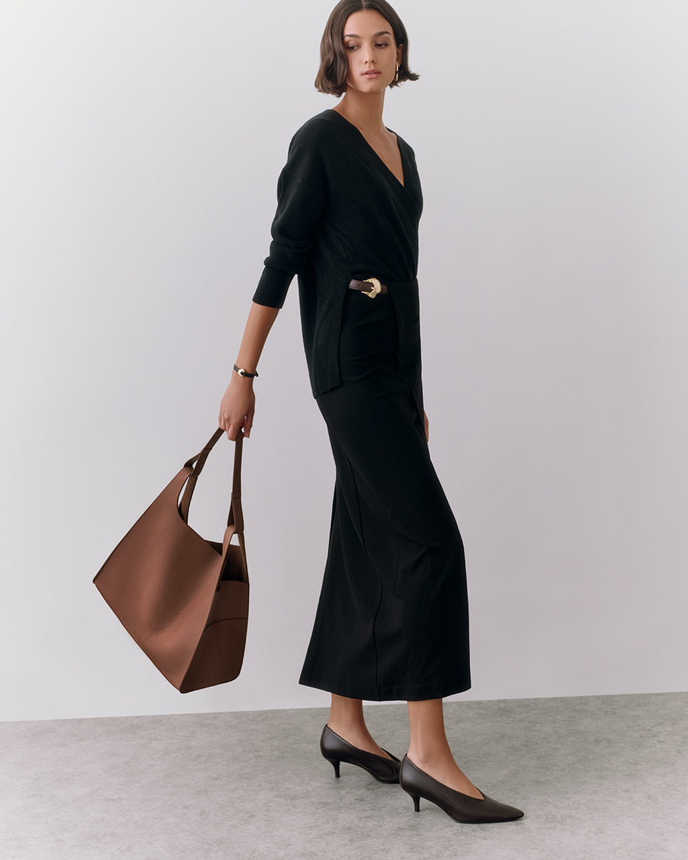 Person in a long dress holding a large bag, standing on a plain surface.