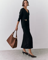 Person in a long dress holding a large bag, standing on a plain surface.