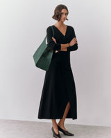 Person in long dress with shoulder bag, standing with arms crossed.