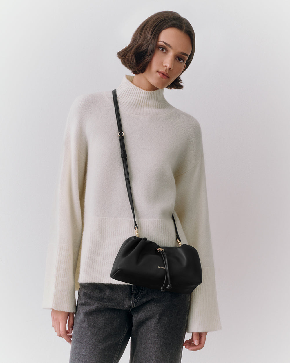 Person wearing a turtleneck sweater and crossbody bag, looking at the camera.