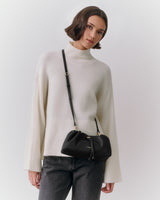 Person wearing a turtleneck sweater and crossbody bag, looking at the camera.