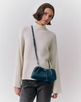 Person wearing a turtleneck sweater with a crossbody bag and jeans.