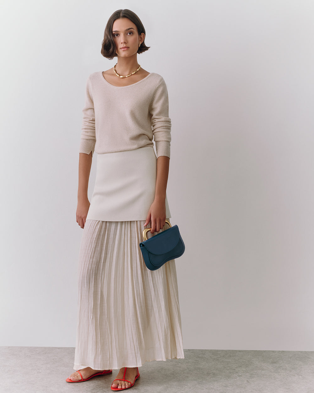 Person wearing a long skirt and top, holding a small bag.