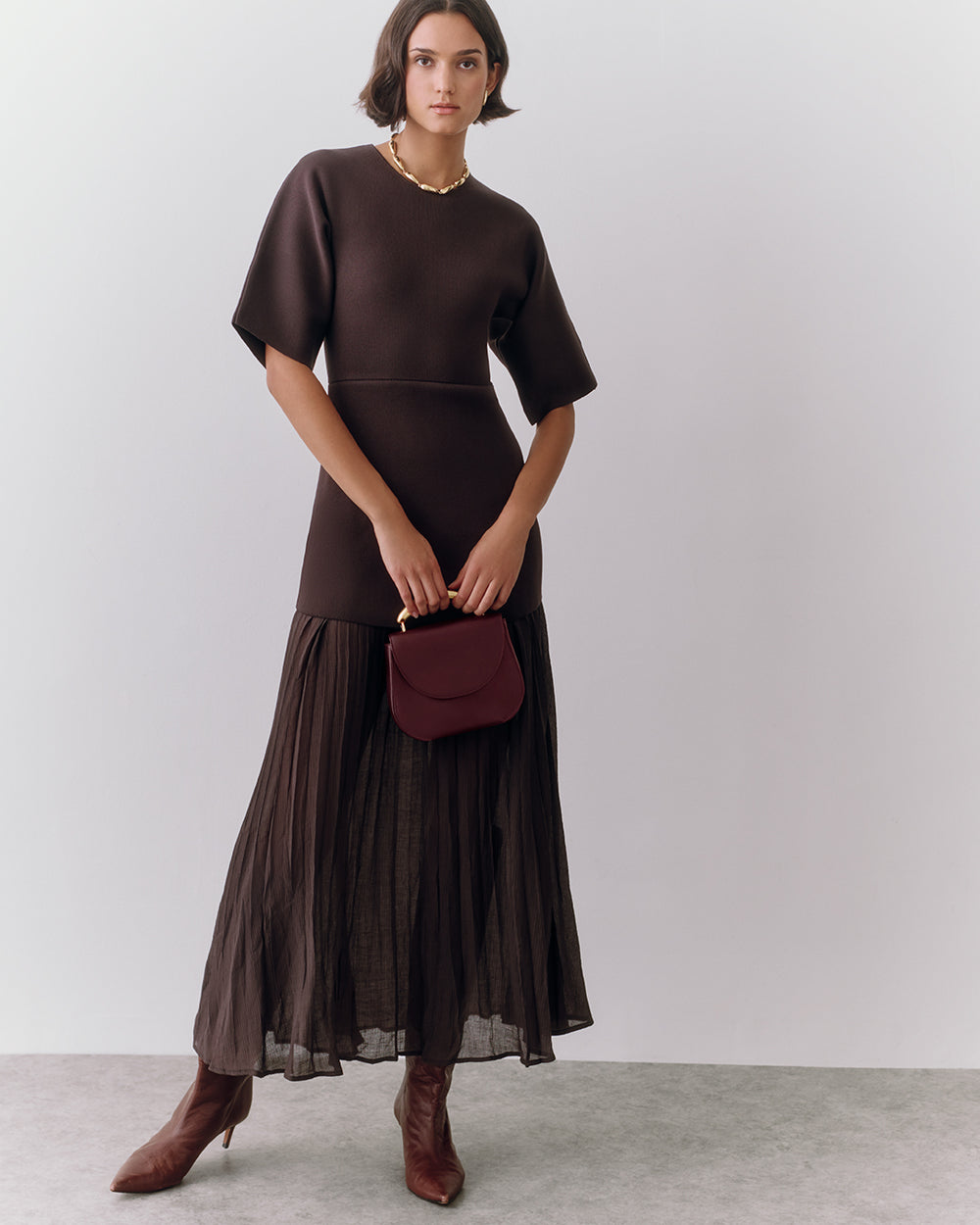 Person in dress holding small handbag, standing, wearing boots.