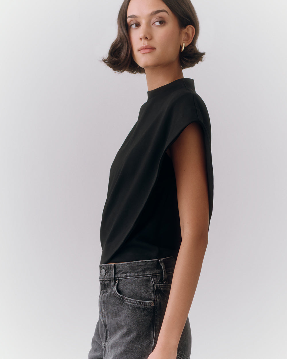 Woman in sleeveless top and jeans standing in profile.