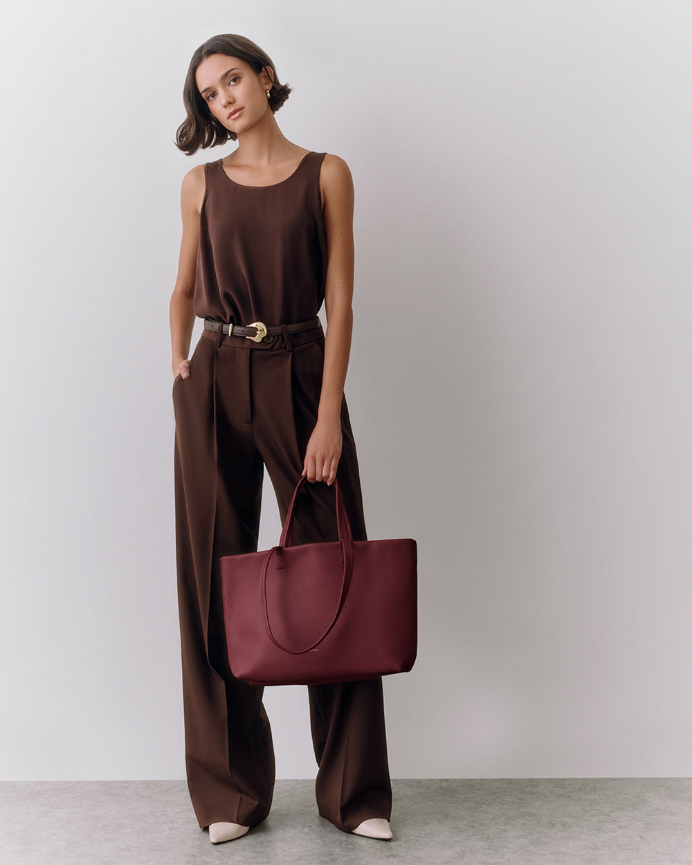 Person wearing a sleeveless top and pants, holding a tote bag.