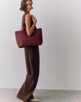 Person wearing a sleeveless top and pants, holding a tote bag.