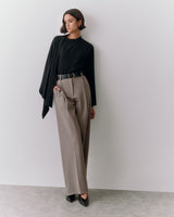 Person wearing a sweater and trousers, standing against a wall.