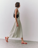 Person in long dress walking with small shoulder bag and sandals.