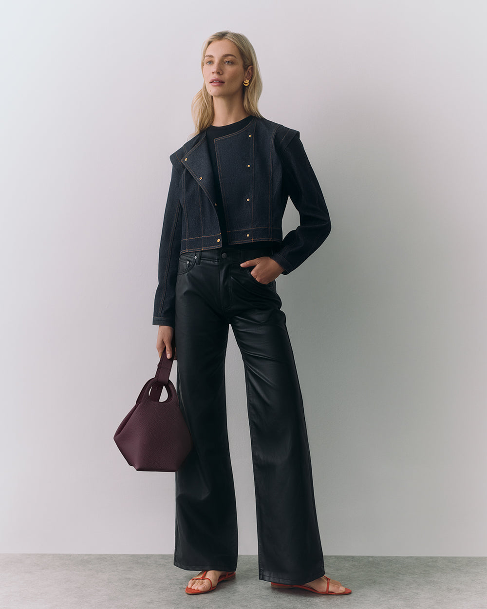 Person in jacket and pants holding a handbag, wearing earrings and sandals.