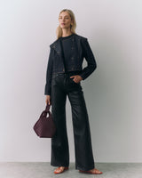 Person in jacket and pants holding a handbag, wearing earrings and sandals.