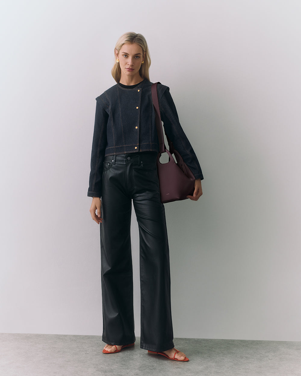 Person standing with a handbag, wearing a jacket and pants.