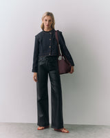 Person standing with a handbag, wearing a jacket and pants.