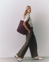 Person standing with large tote bag, wearing a short-sleeve top and wide-leg pants.