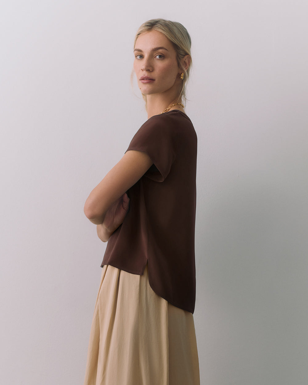 Person in a short sleeve top and long skirt, standing sideways with arms crossed.