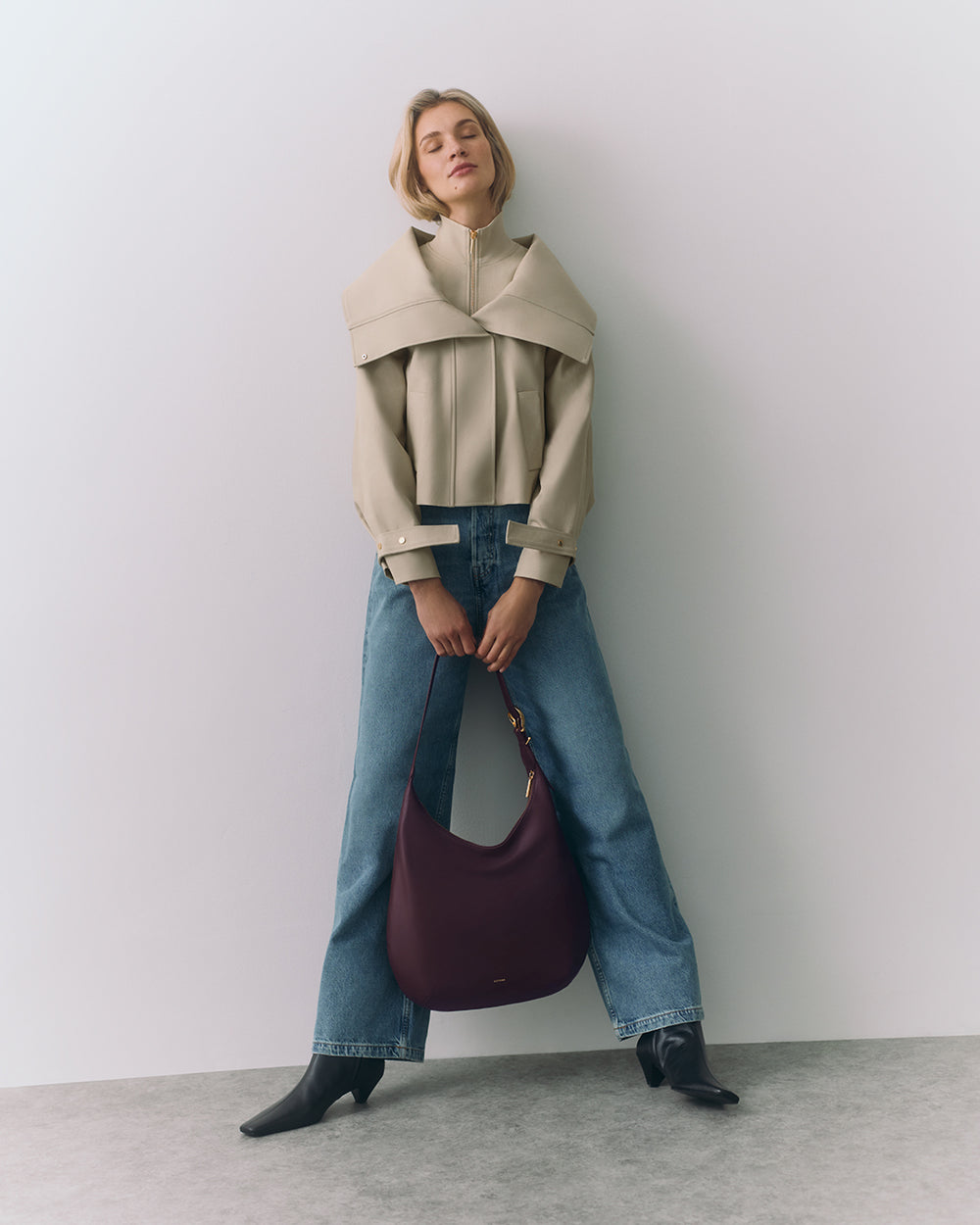 Person posing with a large handbag, wearing jeans, ankle boots, and a structured jacket.