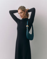Woman in long dress adjusting her hair, holding small shoulder bag