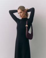 Person in long dress with small shoulder bag adjusts their hair with arms raised