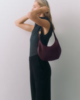 Person standing sideways, holding hair, wearing sleeveless top and holding a handbag.