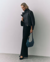 Person in a jacket and pants holding a bag standing against a plain backdrop.