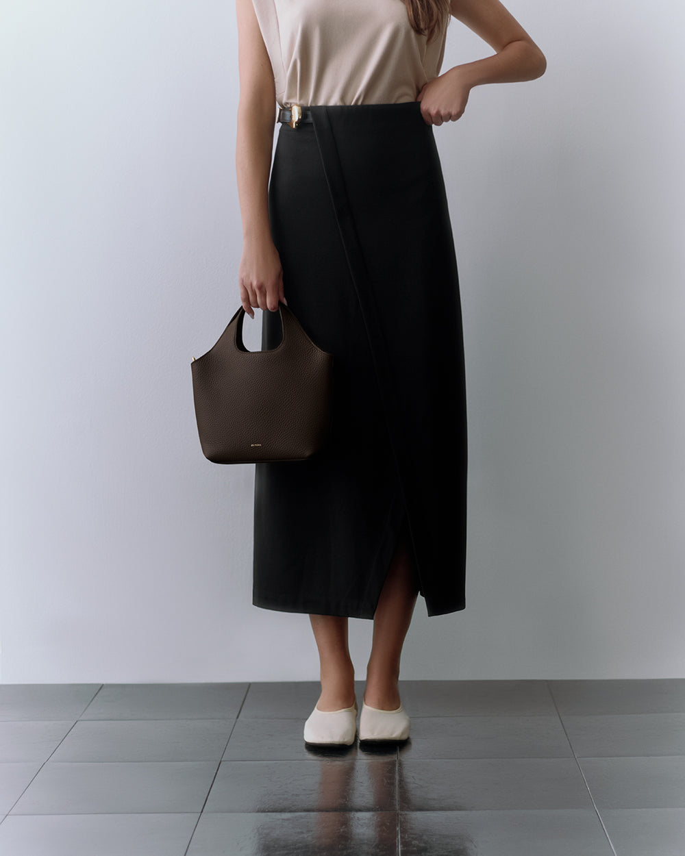 Person holding a bag, wearing a sleeveless top and long skirt, standing on tiled floor.
