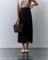 Person holding a bag, wearing a sleeveless top and long skirt, standing on tiled floor.